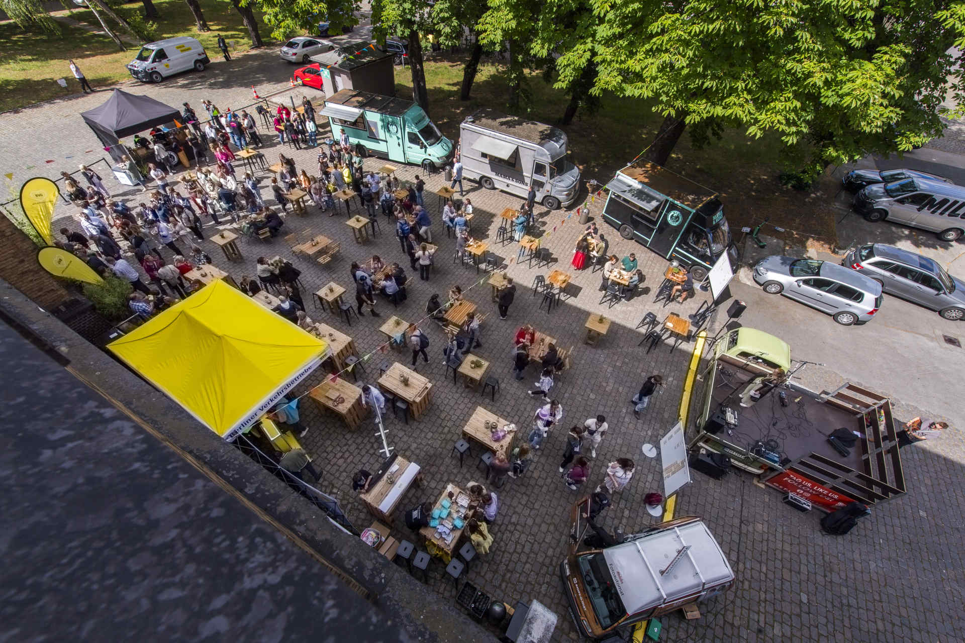 Vogelperspektive auf Außenbereich mit Foodtrucks und Stehtischen und Menschen