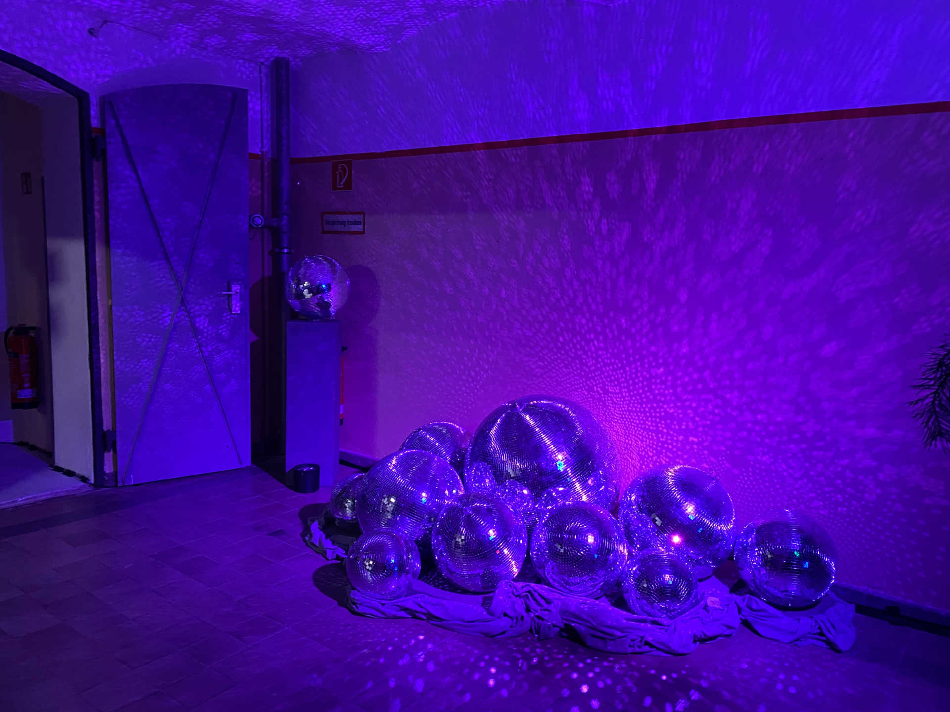 Raum mit einem Haufen Discokugeln auf einem Tuch mit lila Beleuchtung.