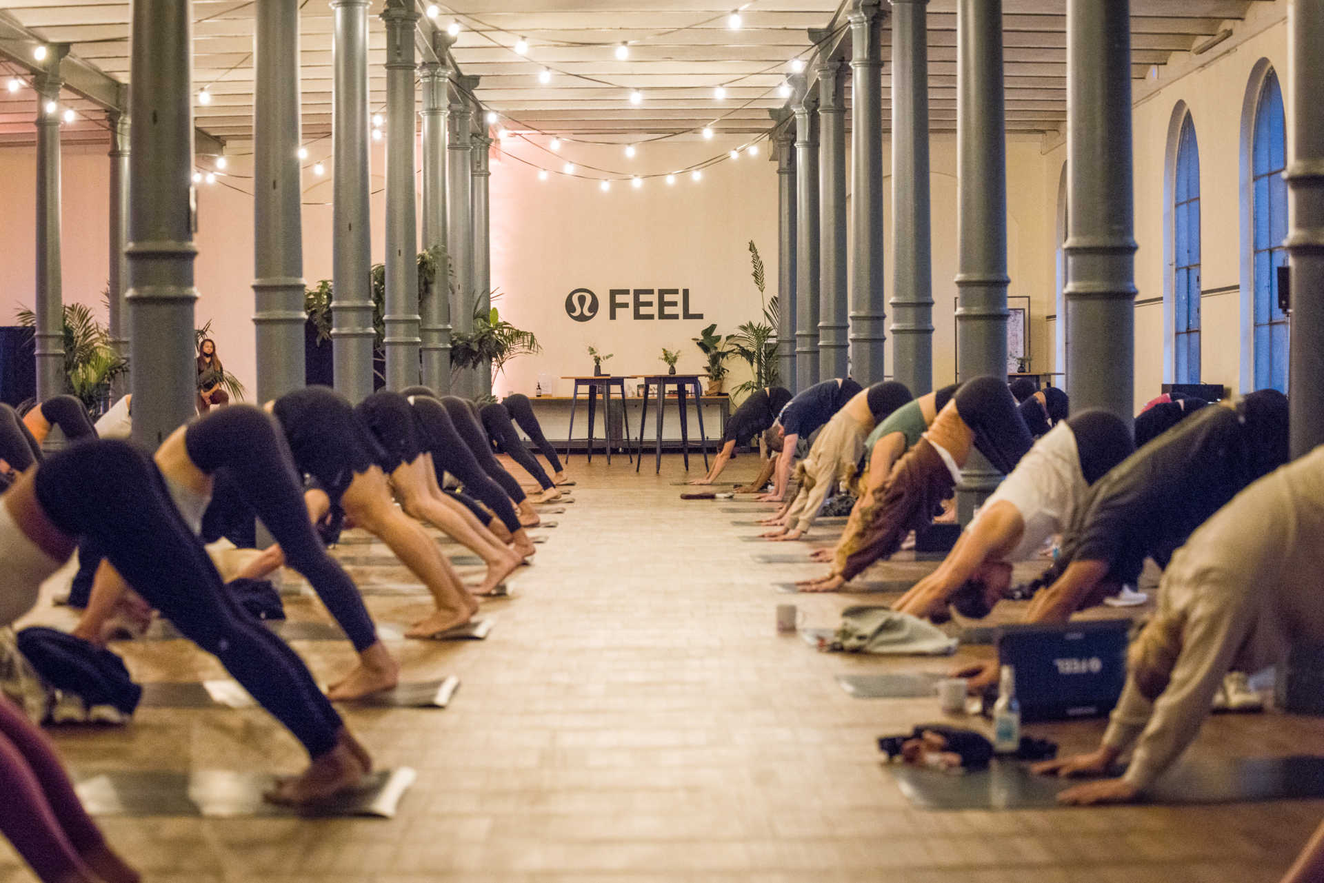Langer industrieller Saal mit vielen Säulen und zwei langen Reihen an Menschen, die Yoga praktizieren.