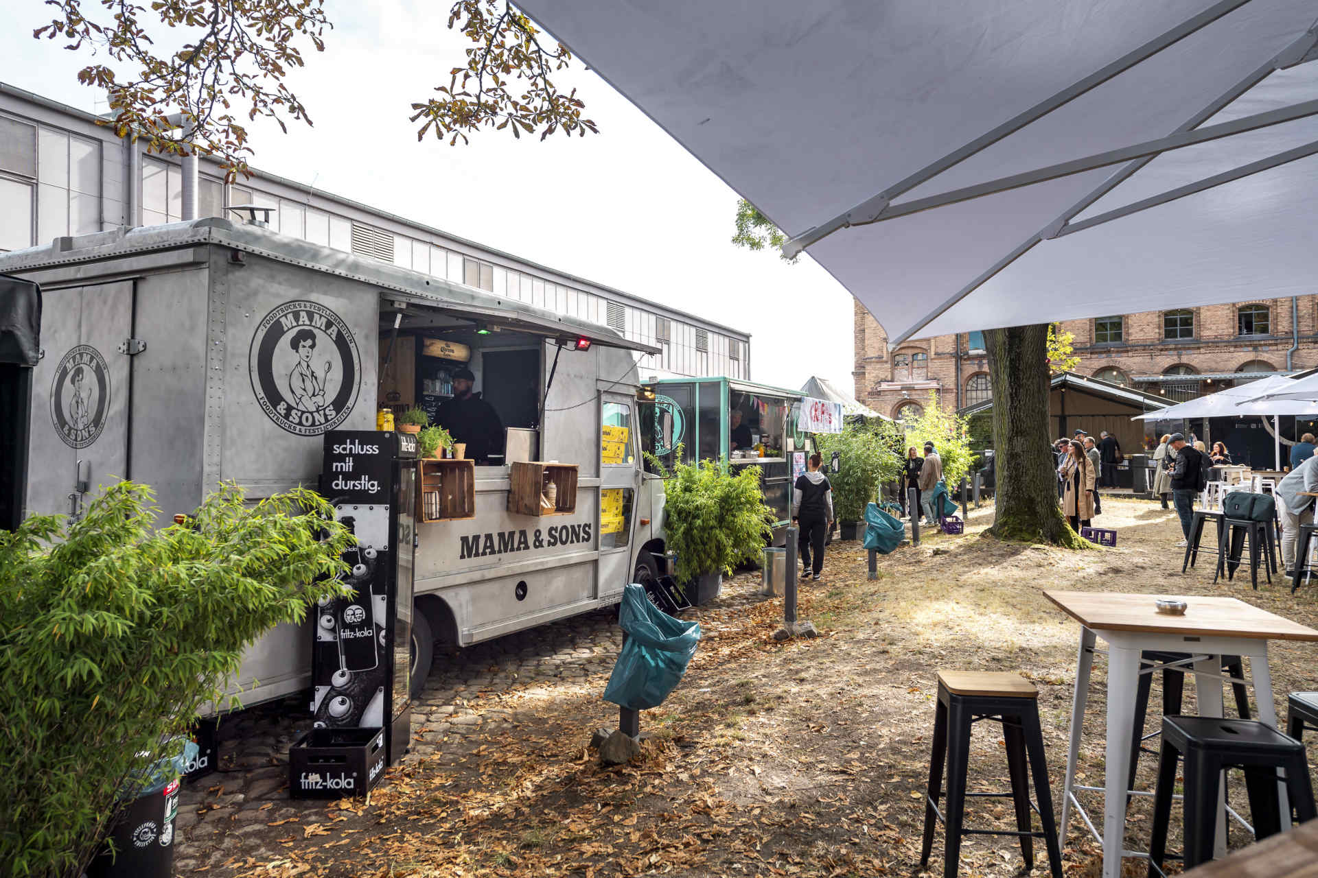 Außenbereich mit Foodtrucks, Stehtischen und Sonnenschirmen