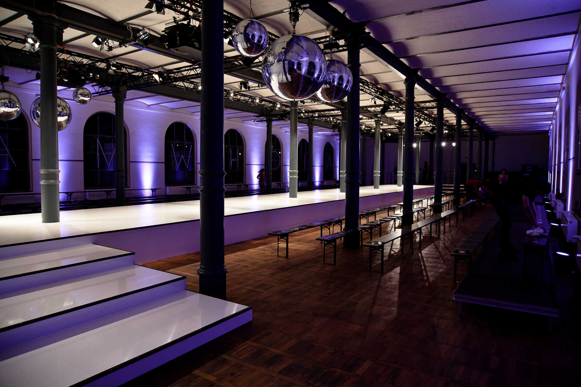 Langer Saal mit weißem Catwalk und großen Discokugeln.