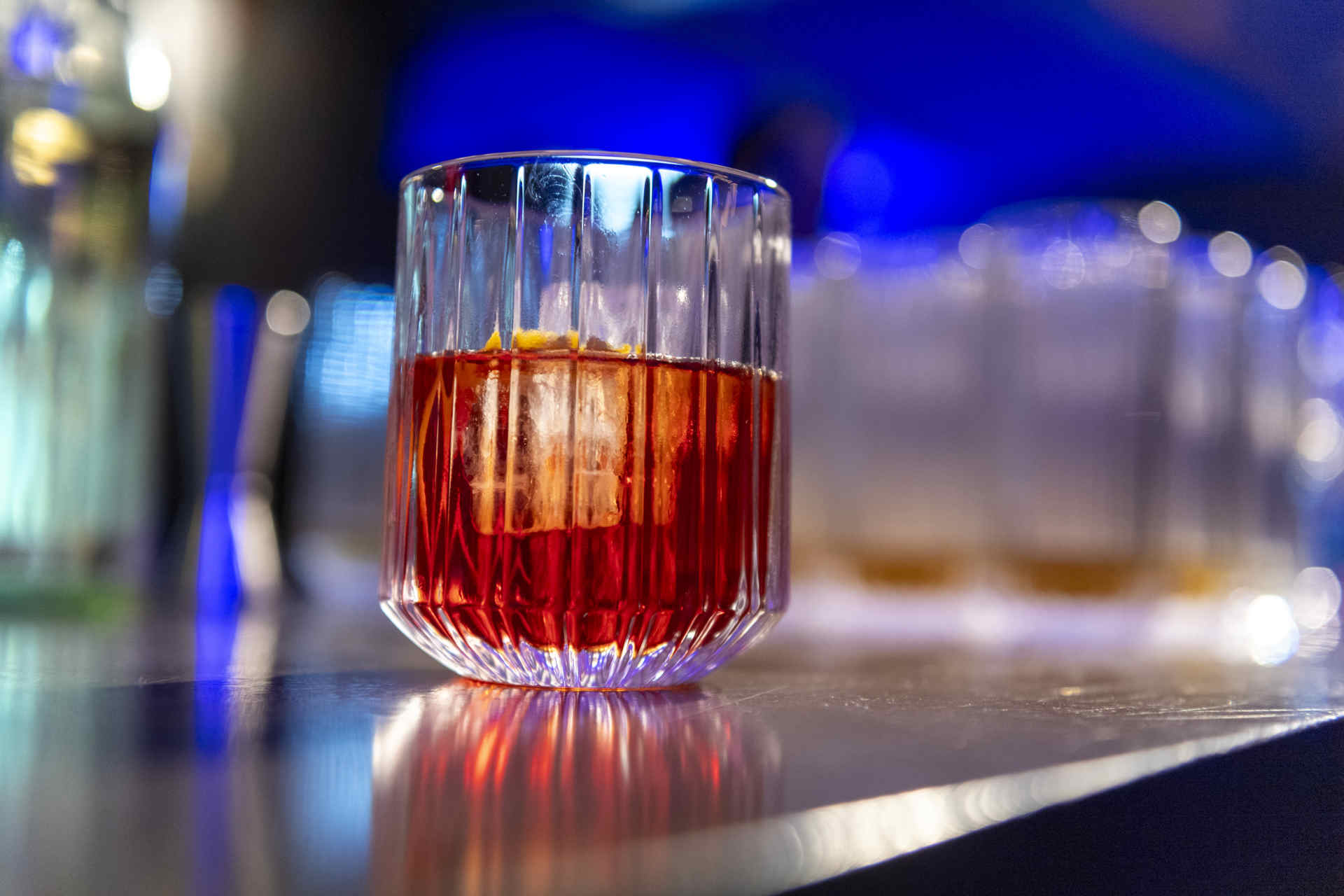 einzelnes Glas auf einer Bar, gefüllt mit orangem Getränk und Eiswürfel
