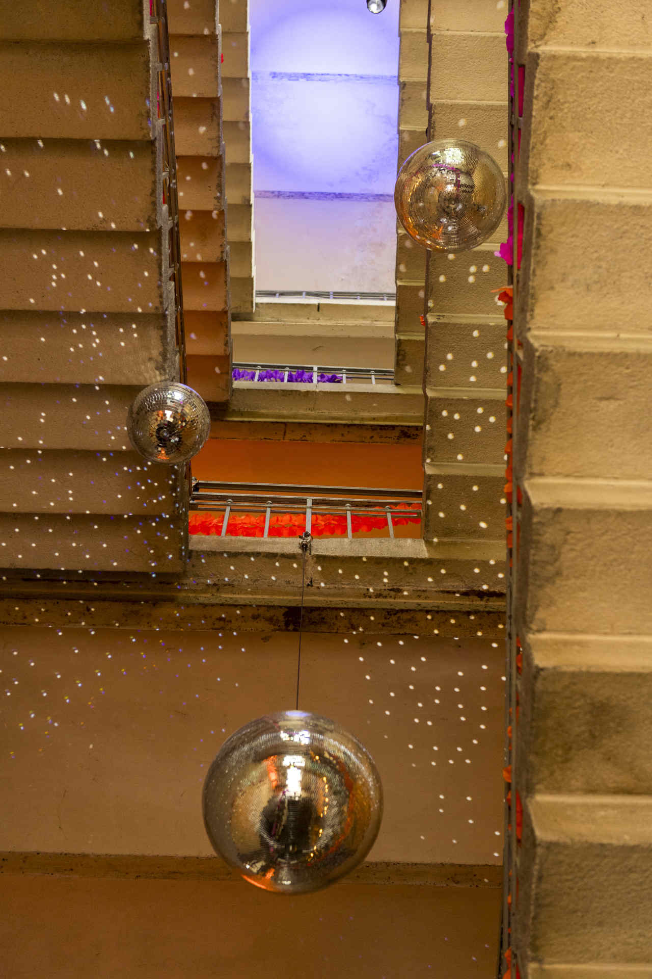 Blick in die Höhe eines Treppenhauses, dekoriert mit mehreren Discokugeln und bunten Girlanden