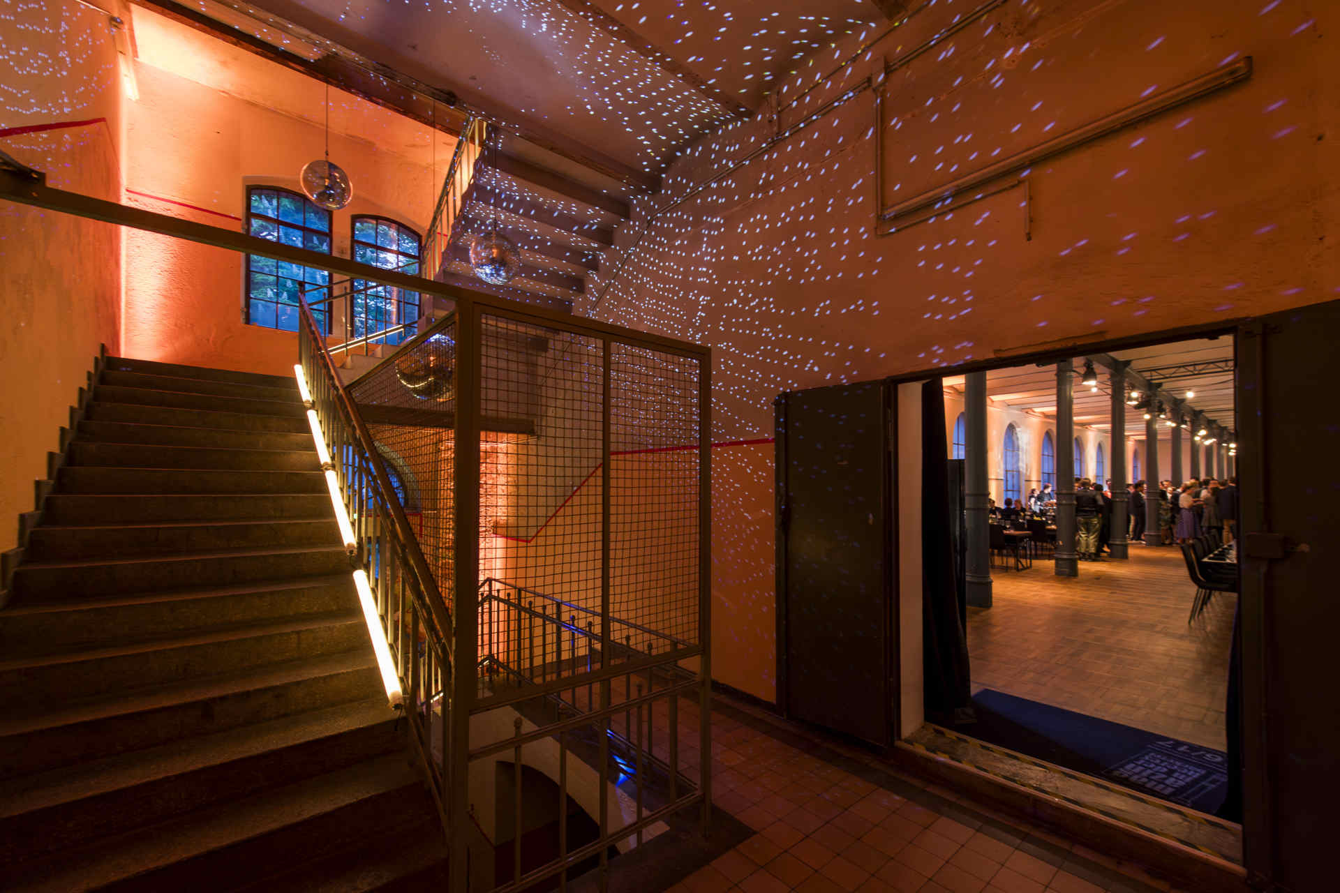 Treppenhaus mit atmosphärischer Beleuchtung und Blick in den Saal