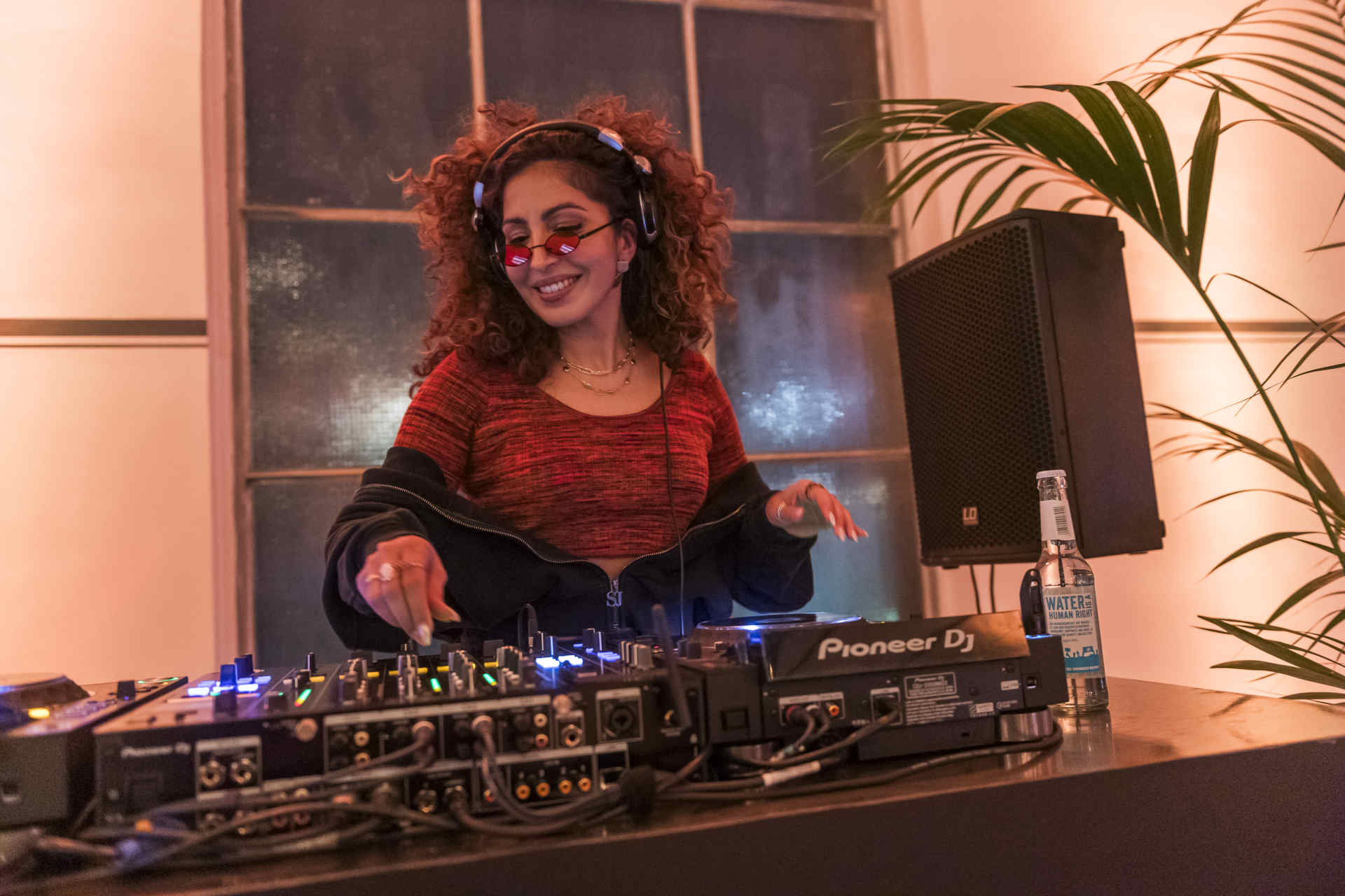 Djane mit Locken und Sonnenbrille legt am Mischpult auf