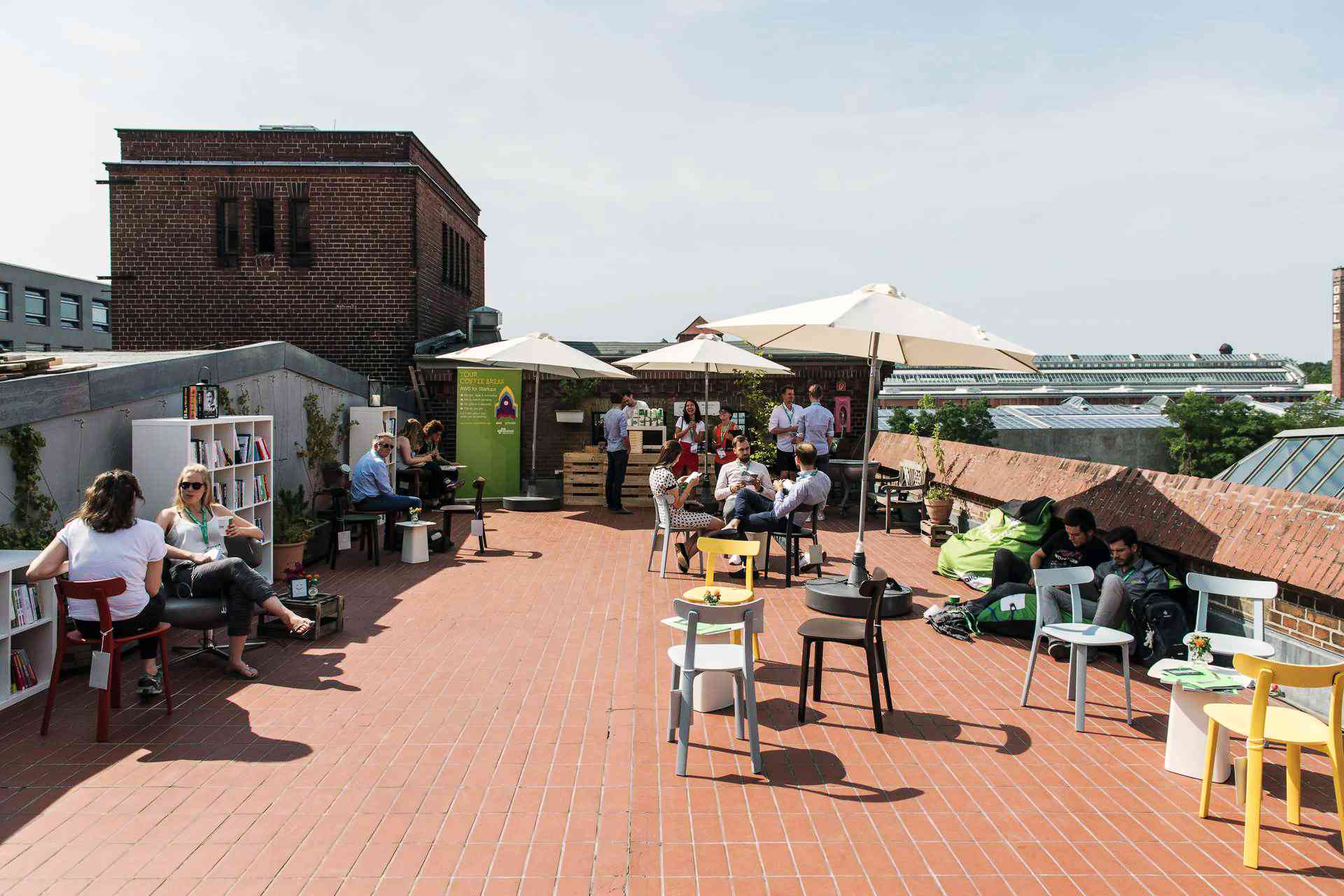 Industrielle Dachterasse mit Bar und Stühlen auf denen Menschen sitzen und sich unterhalten