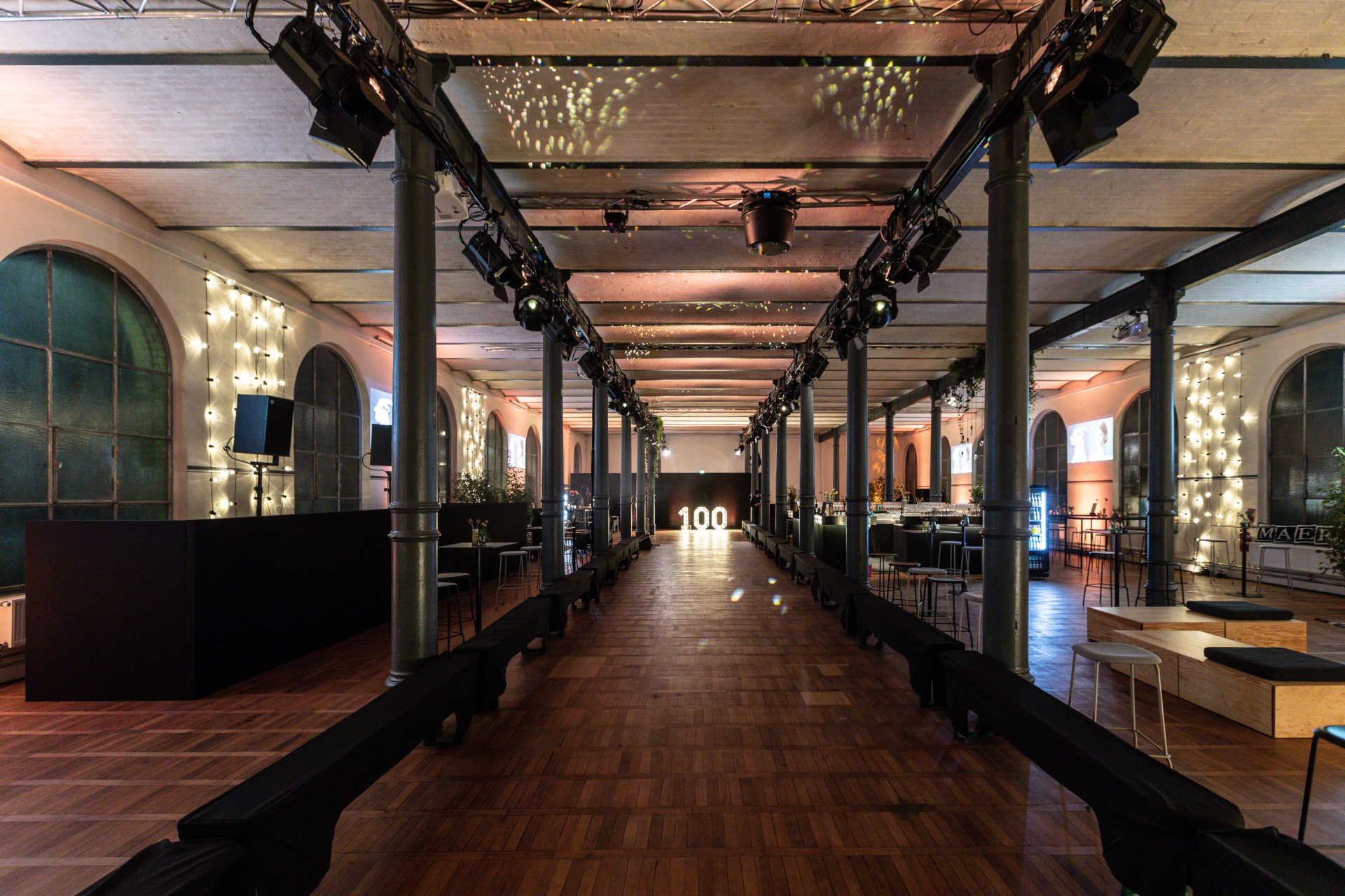 Langer industrieller Saal mit stimmungsvoller Beleuchtung und langem Catwalk und Leuchtschrift.