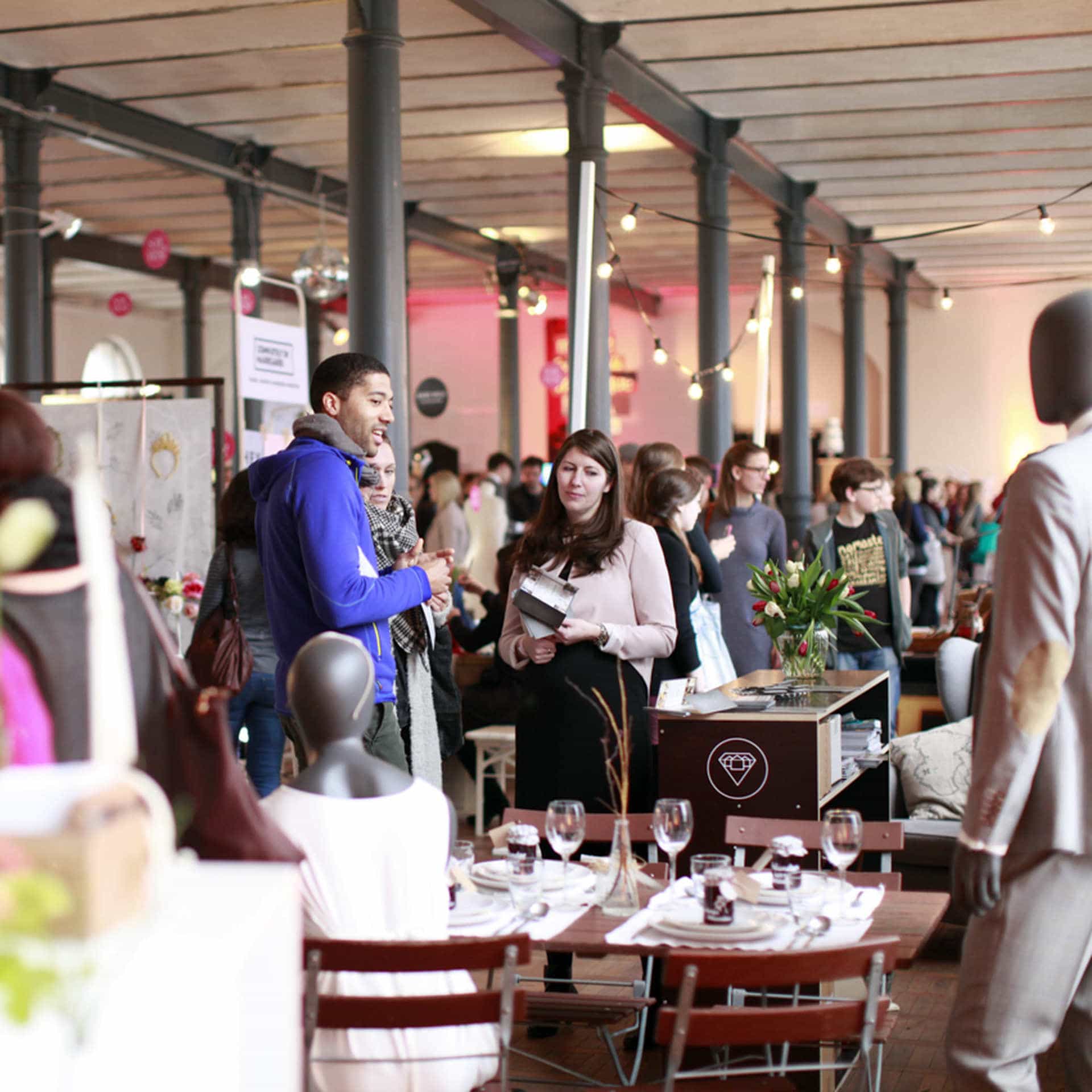 Helmchen Event + Location Magazin Heeresbäckerei Produkt Messe Mehrere Personen stehen in einem großen raum vor ihnen ein gedeckter Tisch