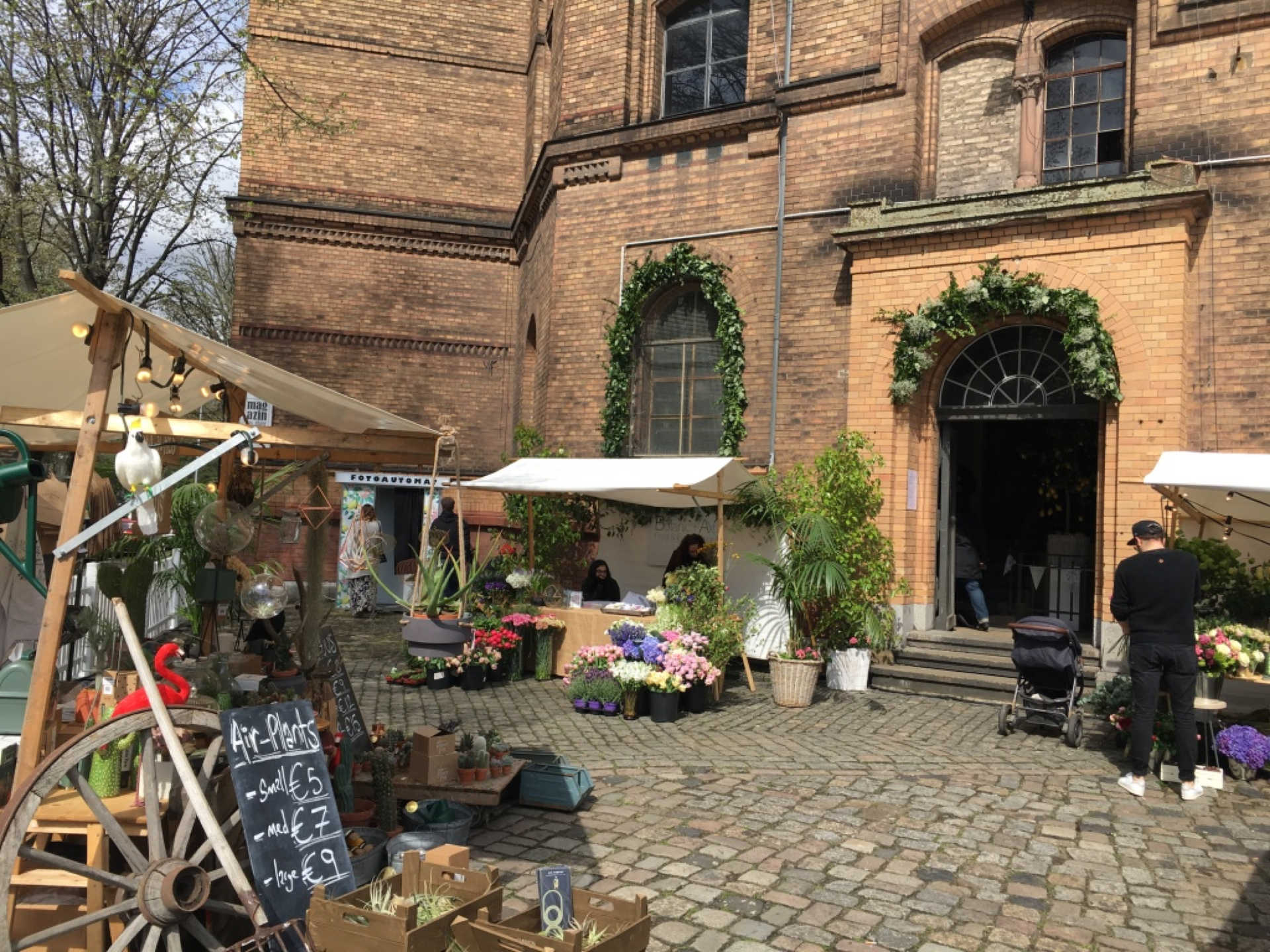 Vorplatz von großem Backsteingebäude mit Marktständen.
